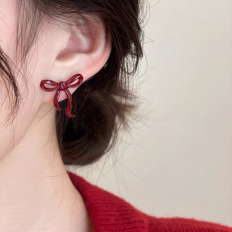 Red bow stud earring shown worn on an ear.