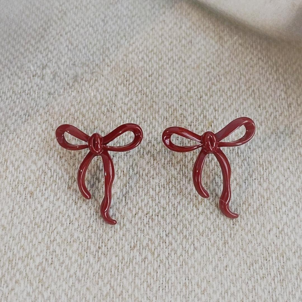 Pair of red bow stud earrings shown from the front on light fabric.