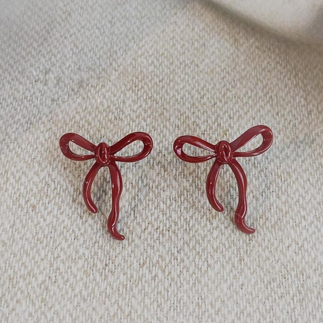 Pair of red bow stud earrings shown from the front on light fabric.