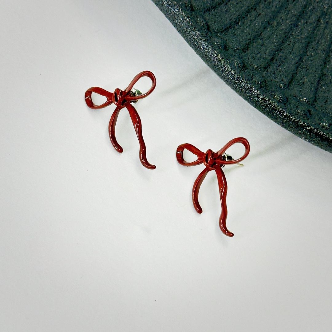 Pair of red bow stud earrings shown at an angle on a light background.